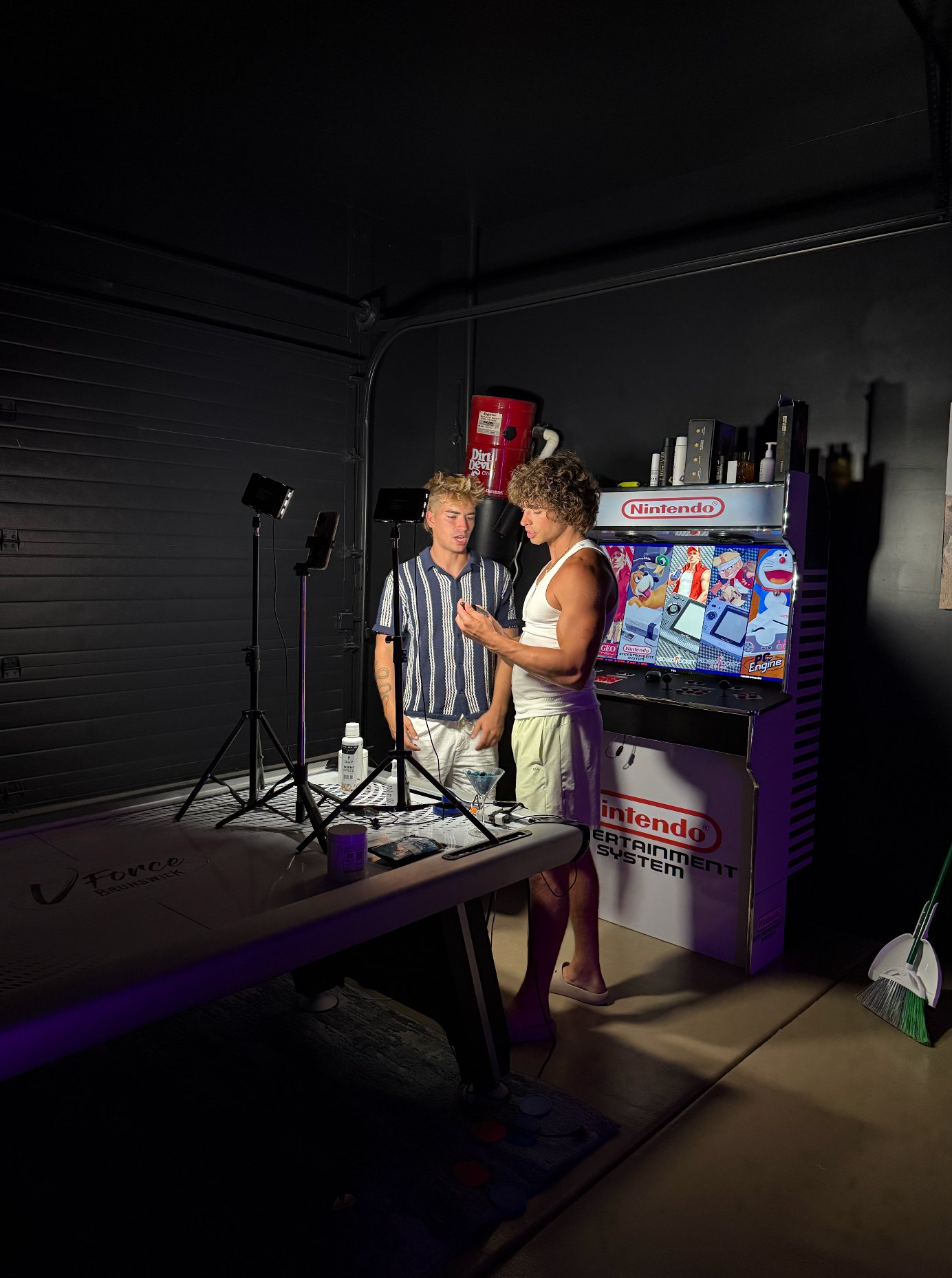 Behind the scenes of an Arizona content shoot, two creators filming a podcast-style setup with lighting and a Nintendo arcade cabinet in the background